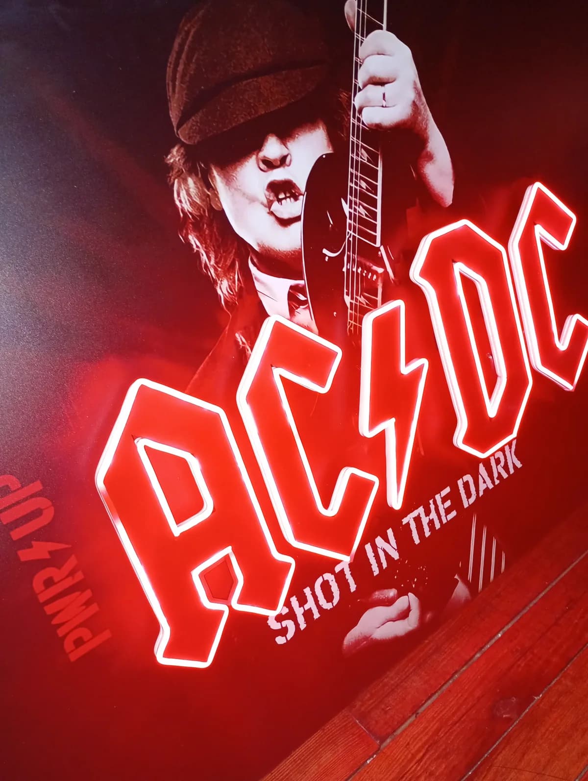 Pieza de AC/DC con el logo y el retrato iluminados por LED, apoyada en el taller